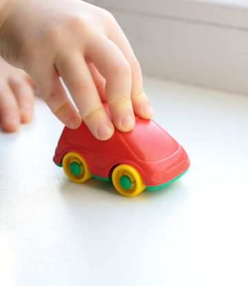 Supply Chain Scene, image of a childs hand on a small, red plastic car