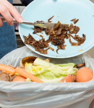 Supply Chain Scene, image of a plate of food being swept in to a wastebasket with other food scraps 