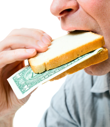 Image of a person eating a sandwich made of money between bread slices 