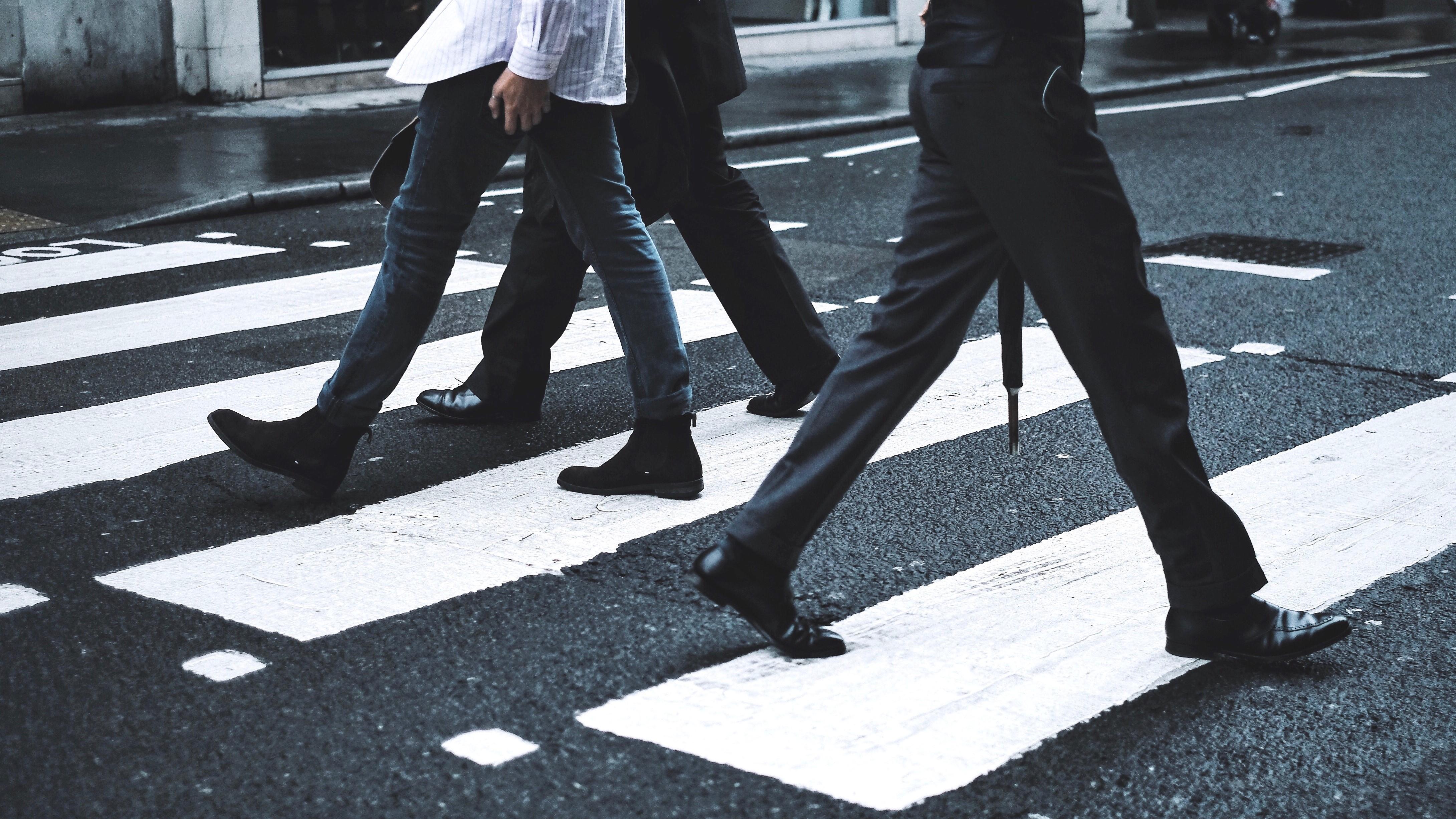 Three people walking across a crosswalk. Mostly black and white color