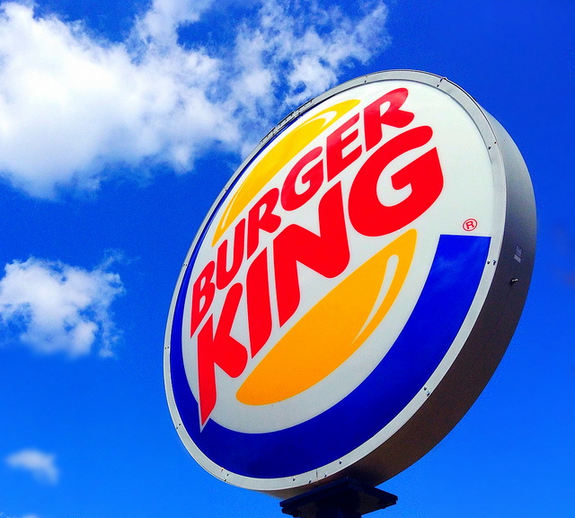 Burger King sign set against blue sky with white clouds.