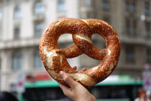 Hand of a person holding a soft pretzel (with building in background)