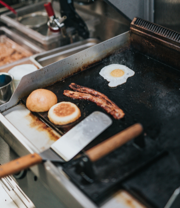 Supply Chain Scene, image of a commercial griddle with eggs, bacon, on it.