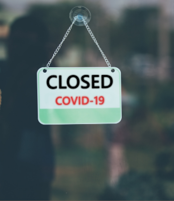 Image of a CLOSED COVID-19 sign hanging on a glass door 