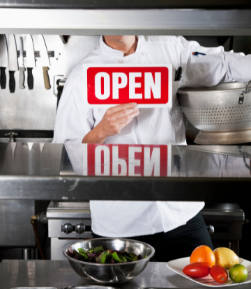 Image of a restaurant chef holding an "Open" sign 